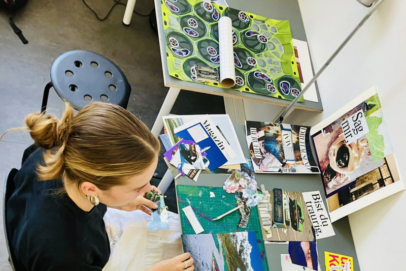 Kursteilnehmerin sitzt am Arbeitstisch und fertigt eine Collage